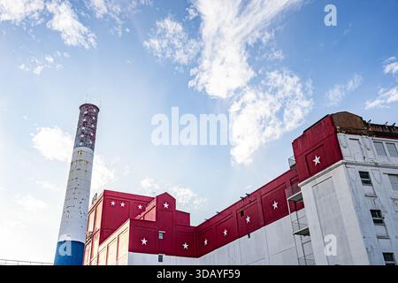 Patriotic red, white, and blue industrial building painted in American flag colors with star-decorated smokestack under blue sky Stock Photo