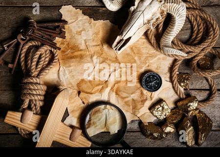 Skull of sheep with travel equipment, treasure map and golden nuggets on brown wooden background Stock Photo