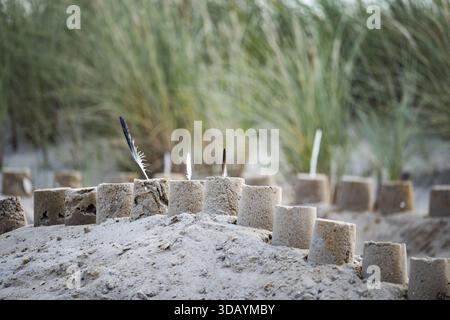 Sandcastle on the beach, detailed view of a sand castle with small towers and dug in the sand, behind it dunes with beach grass in a soft background, Stock Photo