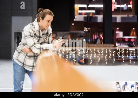 man in plaid shirt leaning on railing and using smartphone in modern shopping mall interior. High quality photo Stock Photo