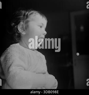 Slavyansk, Ukraine, USSR. An expressive archival portrait from the 1960s capturing a cute toddler boy indoors. The child, dressed in a soft textured shirt, is photographed in profile with his mouth wide open, yawning or singing. The dramatic side lighting creates a strong contrast against the dark background. The black and white image conveys raw emotion, innocence and the atmosphere of a happy childhood in the peaceful industrial city of Donbass during the Thaw era. Stock Photo
