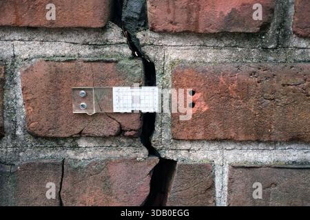 Frontal view of red and brown brick masonry wall with grey mortar, showing a vertical crack extending across multiple bricks. Stock Photo