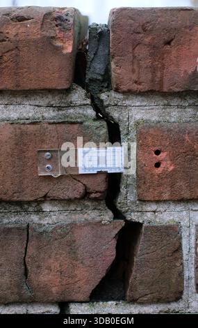 Close-up of brick masonry with wide vertical crack between bricks, exposed mortar, rough weathered surface, natural outdoor light. Stock Photo