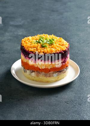 Layered vegetable salad with herring and boiled vegetables on blue background. Stock Photo