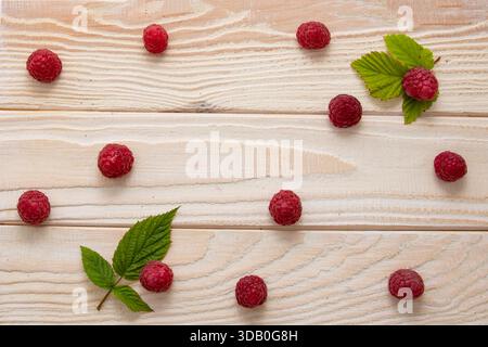 Fresh raspberries with green leaves scattered on light wooden background flat lay Stock Photo