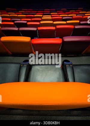 Vibrant, empty cinema or theater seating rows with a colorful gradient of orange, red, and dark leather chairs in the dramatic, dark auditorium ambian Stock Photo