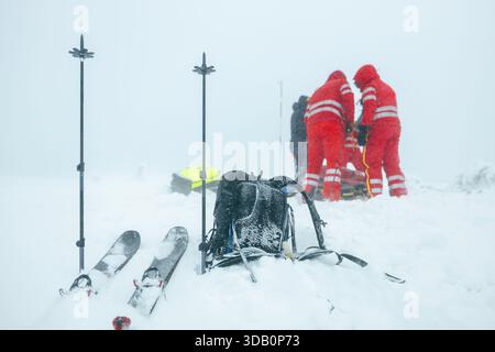 Paramedic team of emergency service helping in mountains in winter during blizzard. Selective focus on ski poles in snow and backpack. Themes rescue i Stock Photo