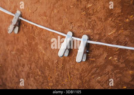 Three metal clothespins clipped on a thin white wire. Textured brown background. Evenly spaced, they cast soft shadows. Stock Photo