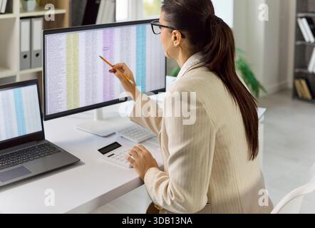 Businesswoman auditing data on large spreadsheet screen while working at desk Stock Photo