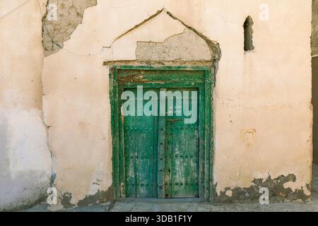 Old green wooden door set in a traditional mud-brick wall in Nizwa, Oman, showcasing historic craftsmanship and the charm of aged architecture. Stock Photo