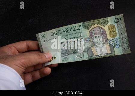 Hand holding Omani rial banknotes of different denominations, showing ...