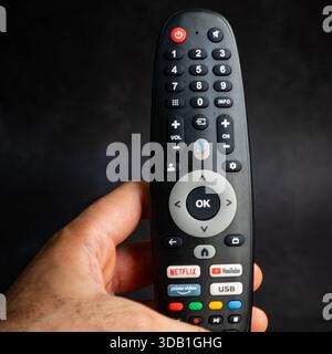 Smart TV remote control held in hand with streaming service buttons like Netflix, YouTube, and Prime Video. Stock Photo