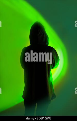 Safe storage of personal data on a smartphone. Shrouded in darkness hooded figure  with phone on vivid neon background. Stock Photo