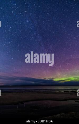 Spectacular night sky showing Milky Way stars and weak aurora borealis dancing on horizon over Baltic Sea coastline in Latvia in December Stock Photo
