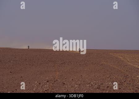 Three motorcyclists racing across a vast Algerian desert plain, kicking up dust in an off-road rally Stock Photo