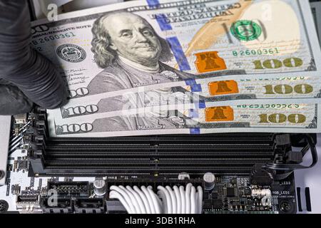 Hands in black gloves inserting 100-dollar bills into empty RAM slots on a motherboard. Conceptual image representing rising tech expenses, costly PC Stock Photo