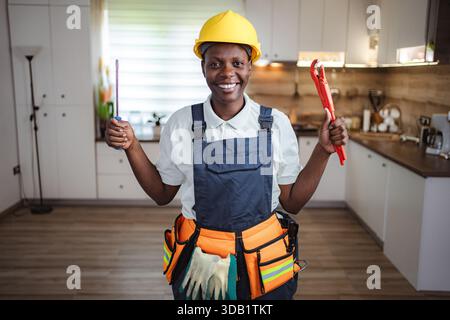 African american female plumber holding wrench and screwdriver smiling at camera Stock Photo