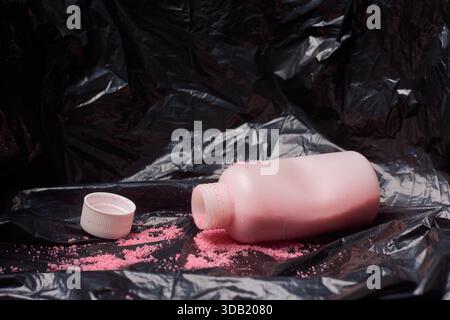 crushed medicine bottle on black garbage bag, spilled pink antibiotic granules and detached white cap, closeup side view, medical waste disposal Stock Photo