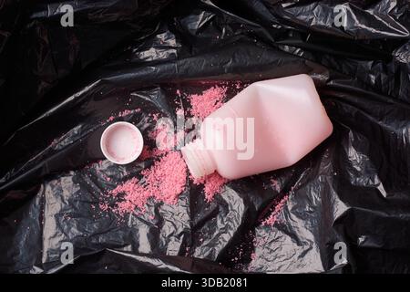 crushed medicine bottle on black garbage bag, spilled pink antibiotic granules and detached white cap, closeup top view, medical waste disposal Stock Photo