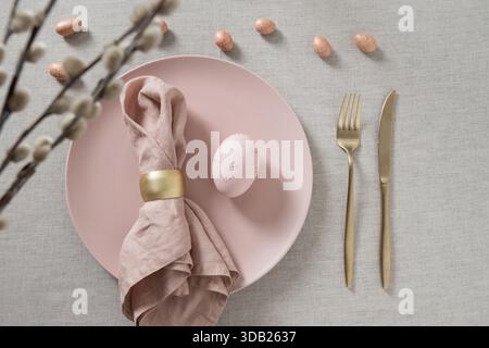 Minimal Easter table setting with pink plates, pastel eggs,willow branches, linen napkin and golden cutlery. Elegant spring holiday table decor with c Stock Photo