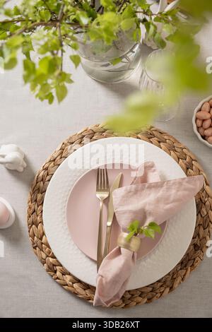 Easter table setting with pink plate, bunny shaped egg holder, pastel candy eggs and spring greenery. Top view .Modern festive dining concept with sof Stock Photo