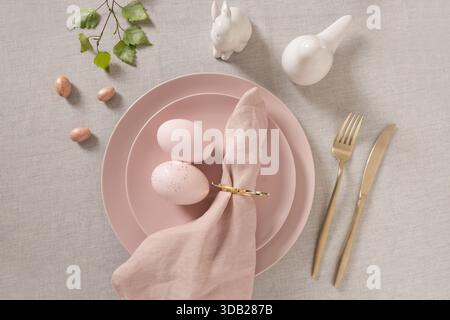 Easter table setting with pink plates, pastel eggs, linen napkin and golden cutlery. Elegant spring holiday table decor with copy space and neutral ba Stock Photo