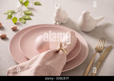 Elegant Easter table setting with pastel pink ceramic plate, gold cutlery, linen napkin and decorative egg. Minimal spring holiday dining concept with Stock Photo