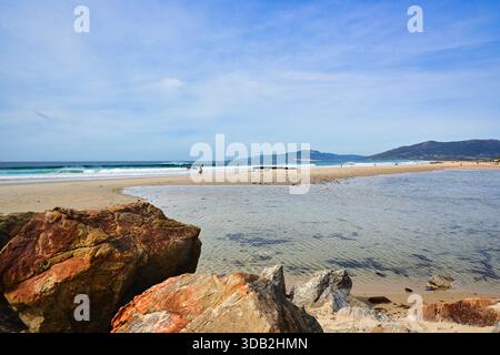 Waves crash on a sandy beach at Tarifa with rocks in the foreground Stock Photo