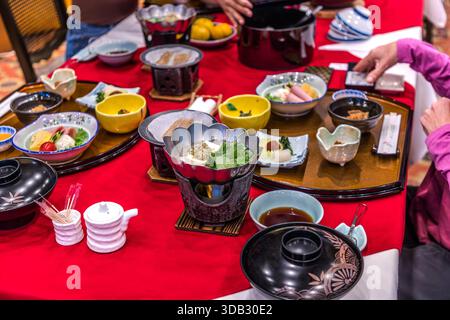 A richly laid Japanese breakfast tray with several small bowls, yellow rice bowls and a tabletop burner for a tofu-and-vegetable dish stands in the dining room of the Watarase Onsen Hotel Sasayuri in the Hongu Valley. The selection of fish, vegetables and rice follows seasonal, regional ingredients. Hongucho Wataze, Tanabe, Wakayama Prefecture, Japan. Stock Photo