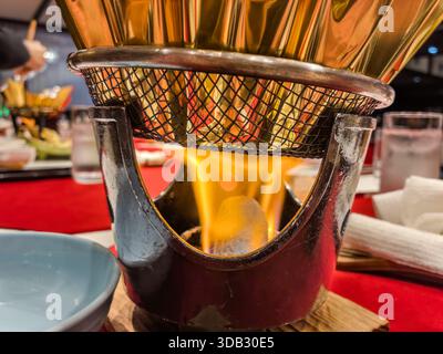 Flames heat a golden pot on the table during dinner at Watarase Onsen Hotel Sasayuri in Hongucho Wataze, Tanabe, Wakayama Prefecture, Japan. Stock Photo