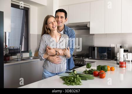Man cuddling woman standing together in modern kitchen Stock Photo