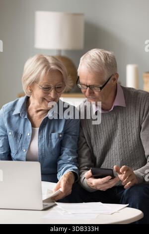 Confident elderly husband wife sitting on couch managing financial documents Stock Photo