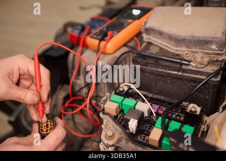 Mechanic accurately measures vehicle wiring with specialized tools, Skilled technician conducts detailed electrical checks on car wiring in workshop Stock Photo