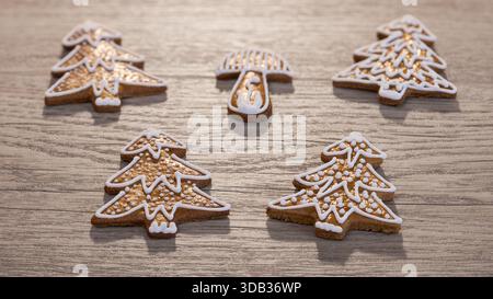 Closeup golden baked gingerbread cookies decorated by icing on wood background. Group of traditional Xmas or New Year sweets in tree or mushroom shape. Stock Photo