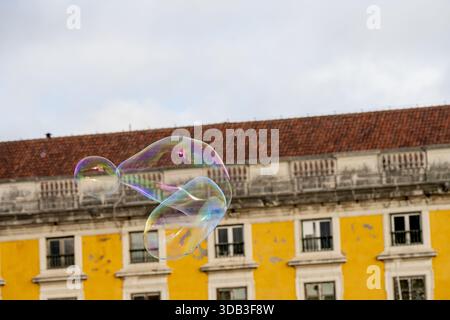 Lisbon Portugal December 05 2025. Soap bubbles float in front of a yellow historic building in the Alfama district during a winter afternoon. Stock Photo
