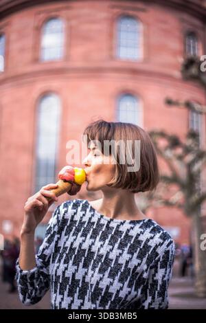 A young woman with shorter hair enjoys a colorful multi-flavor ice cream, captured in profile during a relaxed lifestyle moment. Summer enjoyment. Stock Photo