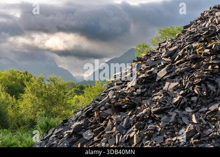 Abandoned slate spoil heap at Glyn Rhonwy quarry in Snowdonia with mountains rising behind under storm cloud Stock Photo