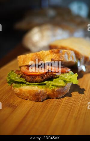 Gourmet beef burger with lettuce and tomato served on crusty bread, photographed on a wooden board with shallow depth of field Stock Photo