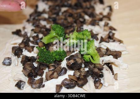 Fresh mushrooms and broccoli are arranged on a layer of cooked chicken on a wooden surface. Someone's hand is reaching toward the food, preparing for Stock Photo