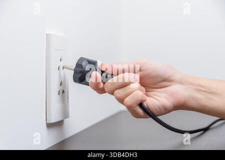 Female hand inserting a black electrical plug into outlet Stock Photo