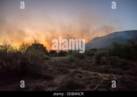 landscape with red clouds of  wildfire smoke on green slopes, shot in dusk light, near Camdeboo, Eastern Cape, South Africa Stock Photo