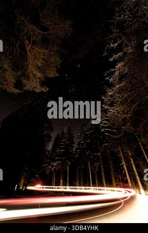 Winding Night Road with Light Trails Through Snowy Pine Forest Under a Starry Sky Stock Photo