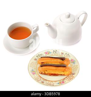 A white porcelain teapot and a matching cup of amber tea are arranged next to two chocolate-glazed éclairs served on an ornate vintage plate. Stock Photo
