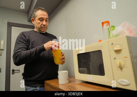 Man opening a bottle next to a microwave in a casual office kitchen or break room Stock Photo