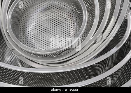 Group of round stainless steel collanders, various sizes, empty and clean, close-up shot, abstract background Stock Photo