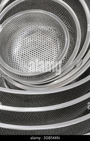 Group of round stainless steel collanders, various sizes, empty and clean, close-up shot, abstract background Stock Photo