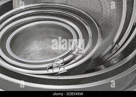 Group of round stainless steel collanders, various sizes, empty and clean, close-up shot, abstract background Stock Photo