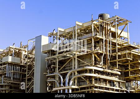 Large industrial plant with steel framework, pipes, and platforms under a clear blue sky, representing energy production and heavy industry. Stock Photo