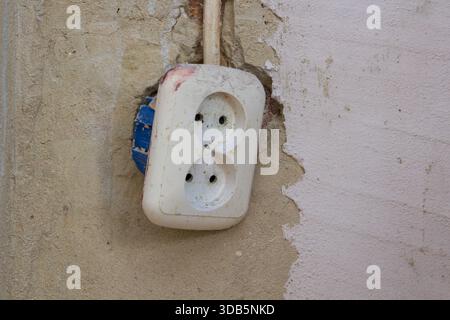 a white double socket hangs on the wall during repair Stock Photo