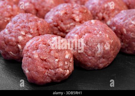 Raw homemade beef meatballs prepared on a black slate cutting board background. Stock Photo